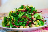 A plate of green salad leaves with grated beetroot and chickpeas.