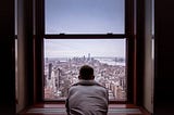 A young man looking out of an apartment window.