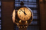 A brass clock with four faces, showing 7 minutes until midnight