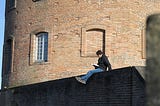 A reader sitting on the eadge of a wall to reading to transform his perspective