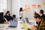 people doing a design workshop, and someone stands on front pointing at sticky notes