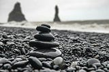 A black and white image of wet stacked stones on a beach