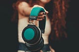 a woman with her arm extended toward the camera holding a pair of headphones as if offering them to you