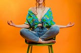 Photo of a girl sitting in a yoga pose against an orange background.