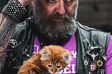 A photo of a Hells Angel member with a black vest, holding a little yellow kitten.