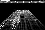 Black and white picture of a skyscraper, photographed from the bottom looking up at the building reaching to the sky.