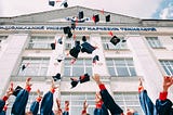 students throwing graduation caps into the air in front of a college building