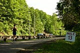 A runner runs along the road. A “Mile 13” sign sits by the side of the path.