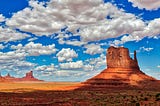 Rock formations in Monument Valley with a blue sky and clouds.