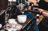 Big coffee machine operating, coffee dripping into a cup.