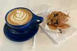 a latte in a blue mug next to a partially eaten muffin