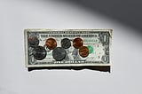 A dollar bill with several coins on top of it.