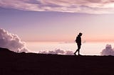 A man walking on a mountain, a pink sunset is displayed behind him