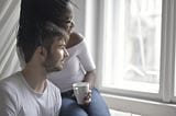 A photo of an interracial couple wearing white shirts, sitting down next to each other while looking out a window