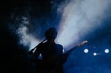 Unknown musician playing guitar on stage with smoke behind them