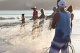 Fishermen cooperating to cast a fishing net