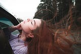 A young woman is enjoying the nature while sitting in a car.