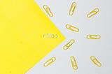 Yellow paperclips are shown on a white surface and one white paperclip is on a yellow surface