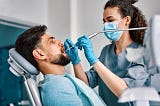 A male patient getting his teeth fixed by a female dentist