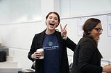 woman with coffee in hand and other hand in peace sign