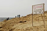 Many people on a dangerous people beyond a sign warning of danger, do not proceed past this point