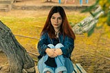 A young woman sitting on a parkbench in front of a playground