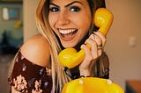 A person on the telephone, holding the receiver to their ear and looking exaggeratedly happy