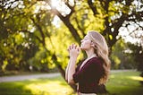 Woman praying outside near trees.