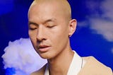 A headshot of KevJumba looking downwards in front of a cloud-printed background