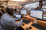 A responder wearing a headset, sitting in front of multiple computer screens