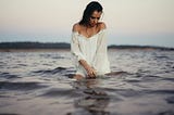 Woman dressed in white, in the ocean, water up her thighs.