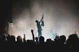 In a picture at a rock concert, a band member is holding up his guitar to the crowd