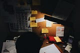 Working at a dark, untidy desk, late at night.