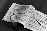 A black and white image of music with a glass next to it.