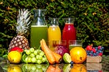 A set up of assorted fruits and what green, orange and beetroot juices and smoothies in transparent bottles.