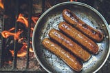 A pan full of cooking sausages on a coal fire grill