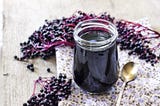 A bunch of elderberries in the background with a jar of elderberry syrup in the foreground