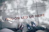 The feet of two people on a sidewalk with “Passion Led Us Here” written on it