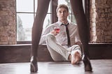 Photo of a Handsome Young Businessman in a suit is holding a glass of wine and looking at the Girl in Lingerie.