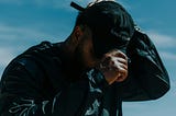 a man outside, wearing a black hat and a black sauna suit, you can see drips of sweat on the outside of the suit on his chest