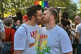 gay couple at pride kissing. Their t-shirts say “I am made in the image of God”