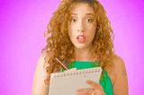 Gif: A blonde woman writing in a notebook and looking up in-between.