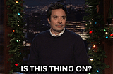 GIF of Jimmy Fallon pretending to tap on a microphone and saying In This Thing On?