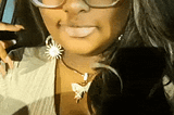 A gif of me from my IG jupiter.dior. I’m wearing a nude top, with a sparkly butterfly necklace, sparkly sun and mood earings, and gold moving butterfly clips in my wig. It’s dark brown with a platinum moneypiece. The filter I am using has gold sparkles cascading down my face. Text says “I got read down today and low key I really needed to hear it 🙃”