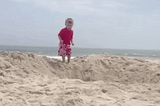 young kid jumping into a big sand hole on the beach
