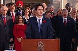 Justin Trudeau shrugging at a press conference. He is standing in front of the members of his cabinet from 2015.