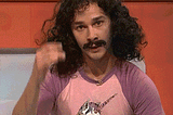 Shia Labeouf saying magic with long hair, a mustache and a unicorn tee shirt