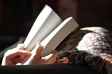 Hands opening a paperback book held on a rug