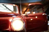 A close-up of a shining headlight on a vintage red car.
