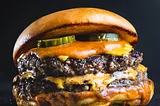 A big juicy hamburger with pickles, cheese, sauce and mustard